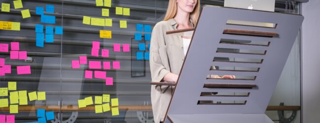 a woman standing in front of a desk with sticky notes on it.